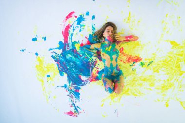 Çıplak bir kadının boya spreyindeki en iyi görüntüsü. Giysisi olmayan bir kız beyaz bir zeminde, renkli lekeler içinde yatıyor..