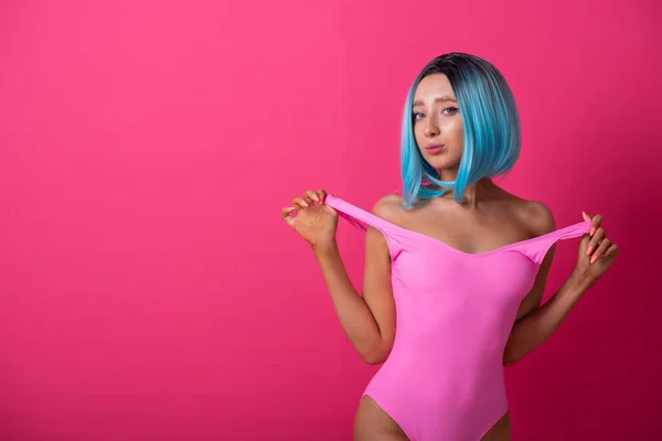 Pretty woman in a pink monokini and blue wig in the studio. Girl with artificial short hair posing in a colored swimsuit. — 스톡 사진