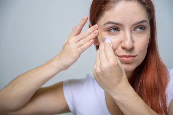 Ritratto Bella donna dai capelli rossi con cinesiologia Ringiovanimento facciale. Ragazza estetista mette sul viso nastro kinesio per lifting facciale . — Foto Stock