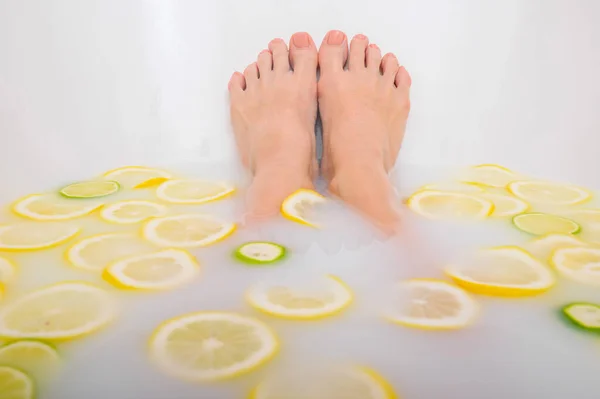 Girl takes a milk bath with lemons and limes. Citrus spa. Body care. Skin whitening. Womens feet. — Stock Photo, Image