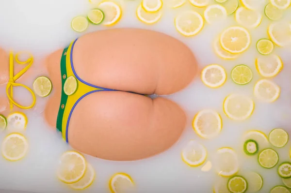 Sarı bikinili tanınmayan kız limon ve limonlu süt banyosu yapıyor. Citrus spa 'sı. Sabunlu suda kadın poposu.. — Stok fotoğraf