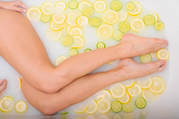 Donna irriconoscibile si fa un bagno al latte con limoni e lime. Citrus spa. Cura del corpo. Sbiancamento della pelle. Gambe femminili vista dall'alto. — Foto Stock