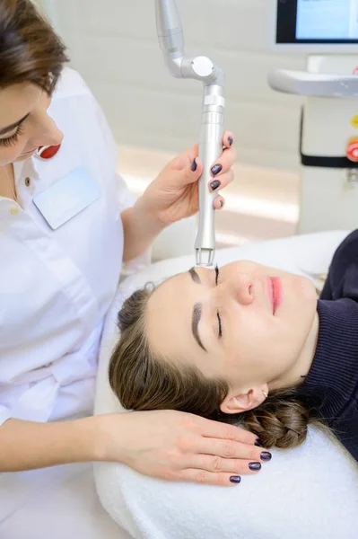 Una mujer se acuesta en un sofá en el consultorio de un dermatólogo y recibe un procedimiento cosmético. Molienda de CO2 de la piel de la cara con la ayuda de un aparato . — Foto de Stock