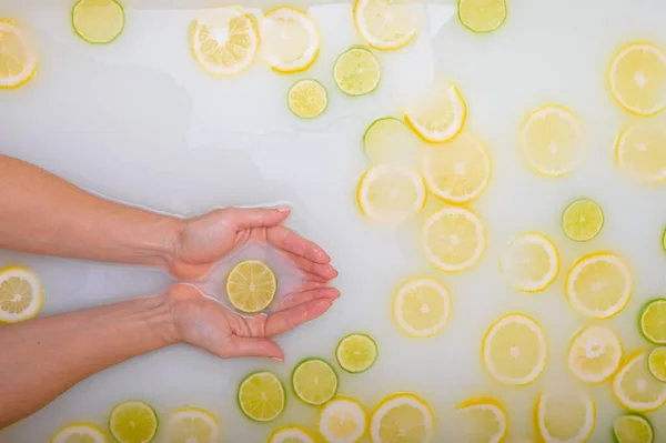 Girl takes a milk bath with lemons and limes. Citrus spa. Body care. Skin whitening. Womens feet. — Stock Photo, Image