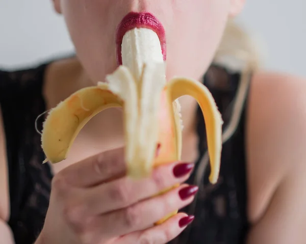 Woman with sensual red lips sucks and licks a banana. Unrecognizable blonde fantasizes about blowjob. Close-up of a female mouth. — Stock Photo, Image