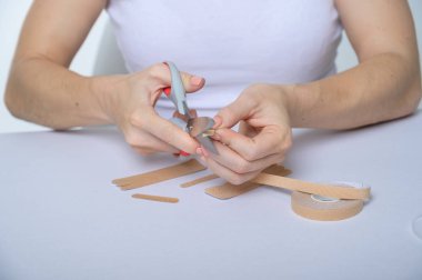 Kadın eli, yüz için yaşlanmadan kalan bir parçayı kesiyor. Kadın elinde yüz gerdirme ve makas için bir kurdele tutuyor..