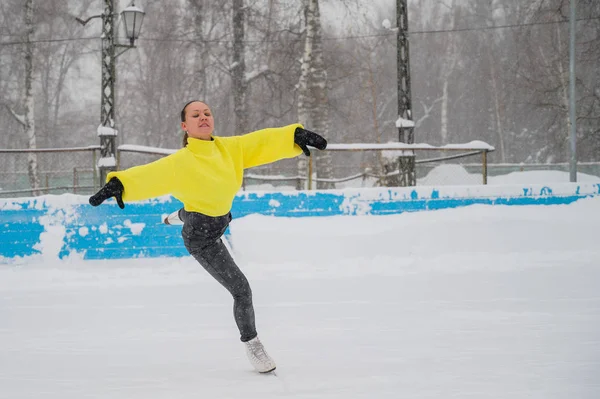 Un giovane pattinatore si allena in una pista di pattinaggio all'aperto a dicembre. Una donna entra per gli sport invernali. — Foto Stock