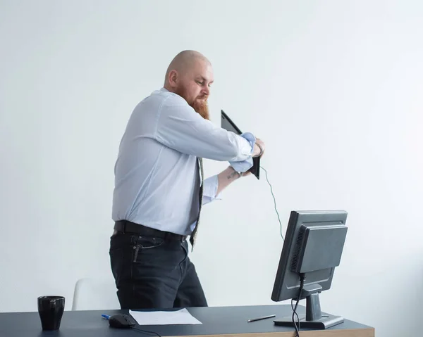 Un calvo enojado con barba roja en la oficina con traje de negocios choca contra una computadora. Manager con una crisis nerviosa rompe el teclado en la pantalla . —  Fotos de Stock