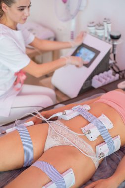 An unrecognizable woman lies on the couch and receives a hardware massage of the abdomen and hips. Weight Loss Procedure. Close-up electric body massage.
