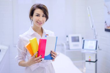 A cosmetologist dermatologist holds in his hands a package with drugs for facial rejuvenation. A female doctor in his office shows injection options.