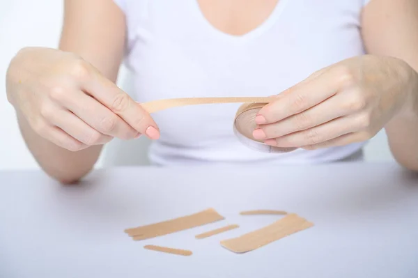 Las manos femeninas se cierran con un yeso contra las arrugas faciales. La chica sin rostro está sosteniendo una cinta en sus manos para un lifting facial. Una mujer irreconocible rejuvenecida con cintas de kinesio . — Foto de Stock