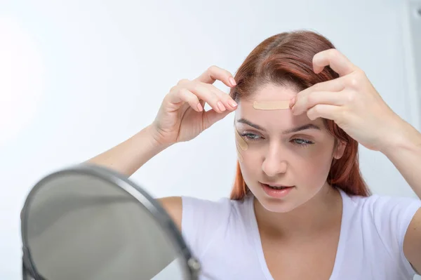 Eine Frau klebt sich ein Kinesiotape auf die Stirn. Das Porträt eines Mädchens macht Applikationen auf ihrem Gesicht gegen Gesichtsfalten. Eine Alternative zu Botox und Hyaluronsäure zu Hause. — Stockfoto