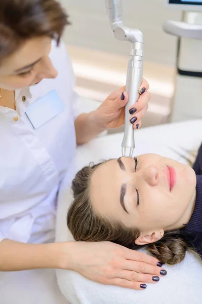 Una mujer se acuesta en un sofá en el consultorio de un dermatólogo y recibe un procedimiento cosmético. Molienda de CO2 de la piel de la cara con la ayuda de un aparato . — Foto de Stock