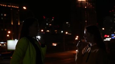 Gece şehrinin arka planında iki kız arkadaş sigara içiyor. Kadınlar gece geç saatlerde sigara ve sigara içerler. Kötü alışkanlık..