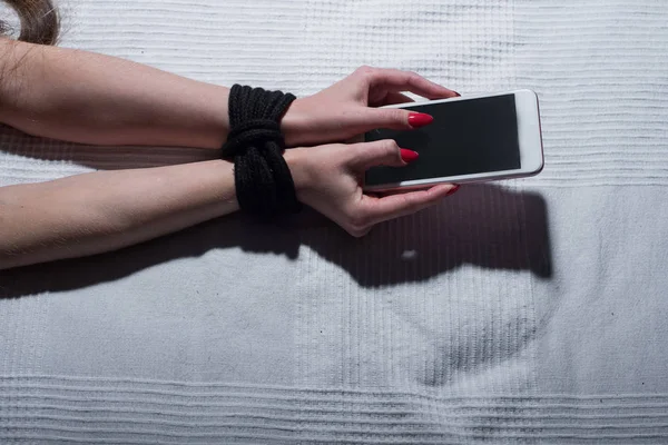 スマートフォンを持っている女性の縛られた手のクローズアップ。携帯電話やガジェットによっては. — ストック写真