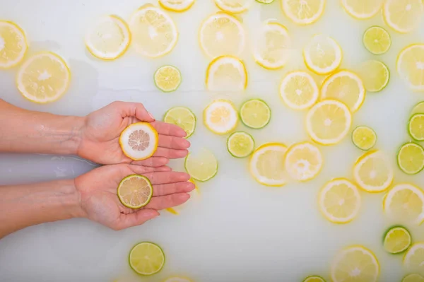 Une tranche de citron vert mûr dans les mains d'une femme. Vue de dessus Fille méconnaissable prend un bain de lait avec des citrons. Spa aux agrumes. Soins du corps. Blanchiment de la peau . — Photo