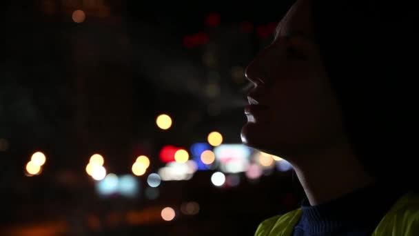 Девушка курит сигарету на фоне ночного города. Женщина страдает никотиновой зависимостью. Плохая привычка . — стоковое видео