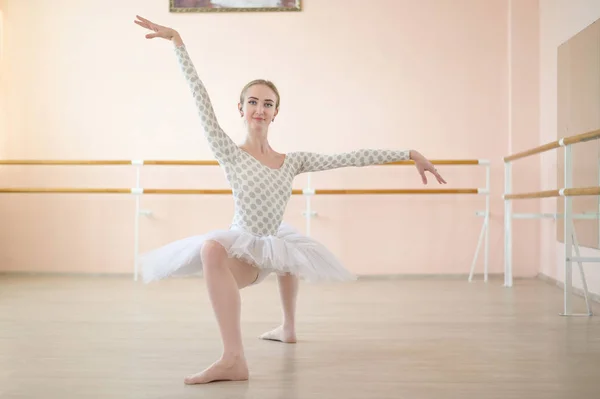 Una bailarina muy flexible en un tutú está de pie en un plie en una clase con máquinas de ballet. Increíblemente bailarina de plástico . —  Fotos de Stock