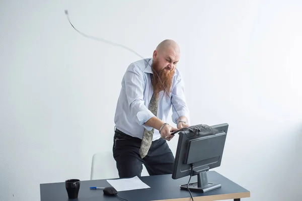 Arg skallig man med rött skägg på kontoret i kostym kraschar en dator. Manager med ett nervöst sammanbrott bryter tangentbordet på skärmen. — Stockfoto