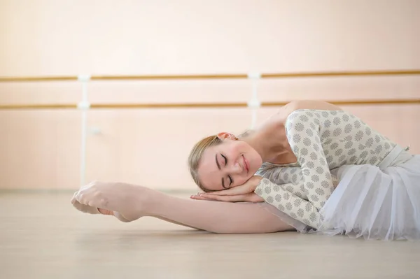 Bela bailarina está treinando em uma aula de dança. Jovem dançarina flexível posando em sapatos pontiagudos. Uma mulher em um corpo e um tutu branco dança uma dança clássica. — Fotografia de Stock