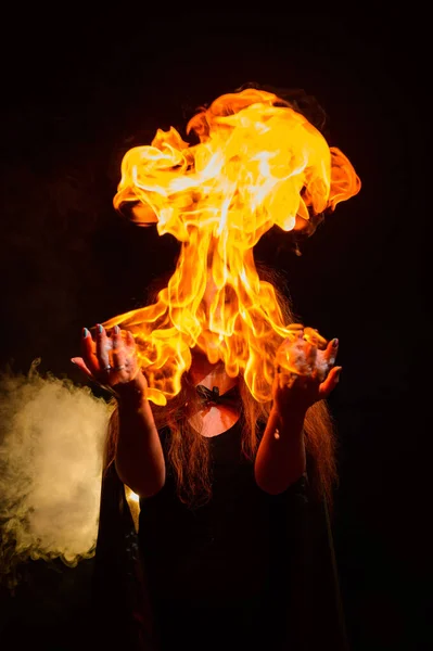 Uzun kıvırcık saçlı bir cadı sihirli bir ateş tutar. Kızıl saçlı bir kadının avuçlarında alev dilleri. — Stok fotoğraf
