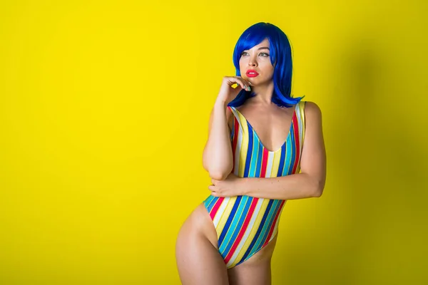 Beautiful woman in a striped swimsuit in a blue wig posing on a yellow background. Portrait of a glamorous girl. — 스톡 사진