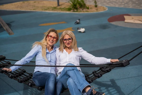 Žena středního věku a její starší matka se houpají v houpací síti. Špatné vidění je dědičné. Větrný den. Babička a matka. — Stock fotografie