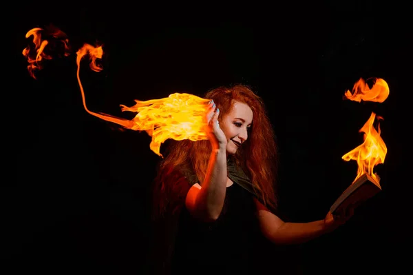 Una bruja ominosa con el pelo largo y rizado sostiene un fuego mágico. Lenguas de llama en las palmas de una mujer pelirroja sonriente. Brujería . —  Fotos de Stock