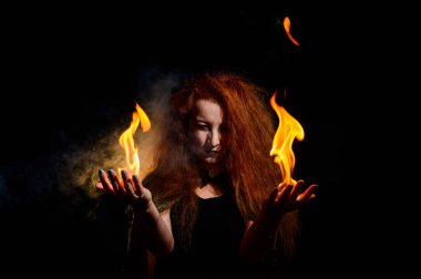 Uzun kıvırcık saçlı uğursuz bir cadı sihirli bir ateş tutuyor. Kızıl saçlı sırıtan bir kadının avuçlarında alev dilleri. Büyücülük..