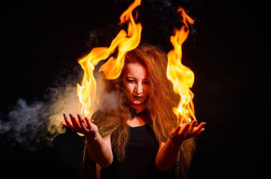 Uzun kıvırcık saçlı uğursuz bir cadı sihirli bir ateş tutuyor. Kızıl saçlı sırıtan bir kadının avuçlarında alev dilleri. Büyücülük..