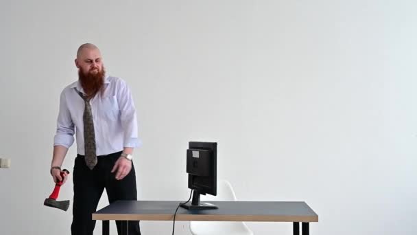 Злой лысый мужчина с рыжей бородой в офисе в деловом костюме разбивает топор компьютером. Менеджер с нервным срывом сломал монитор . — стоковое видео