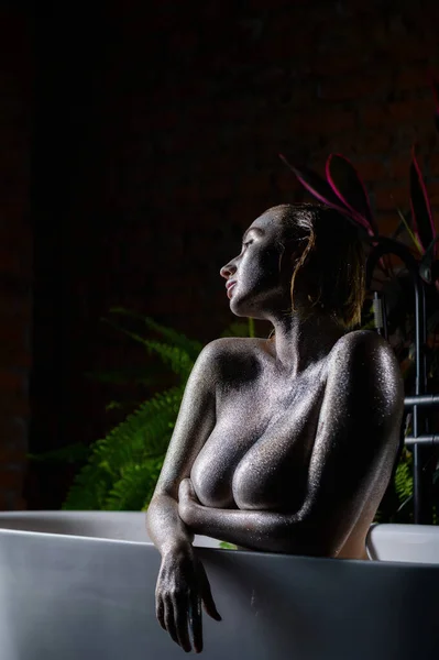 Nackte Frau mit sehr großen Brüsten und silbernem Body im Badezimmer. Ein Mädchen mit einer extragroßen Oberweite mit Funkeln auf der Haut duscht. — Stockfoto