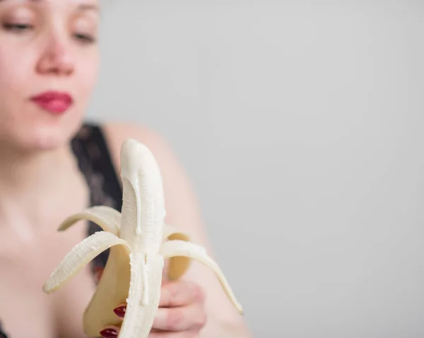 Una bionda in lingerie nera di pizzo succhia e lecca seducentemente una banana. Donna con sensuale rosso imita piacere orale . — Foto Stock