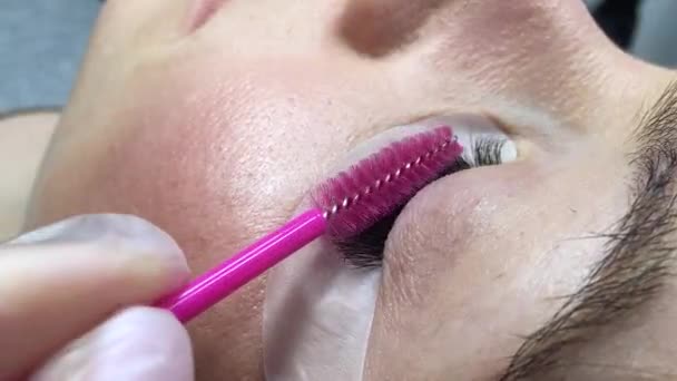 Onherkenbare vrouw oog close-up op wimper uitbreiding procedure. Gehakte video. Master borstelen klanten kunstmatige wimpers. — Stockvideo