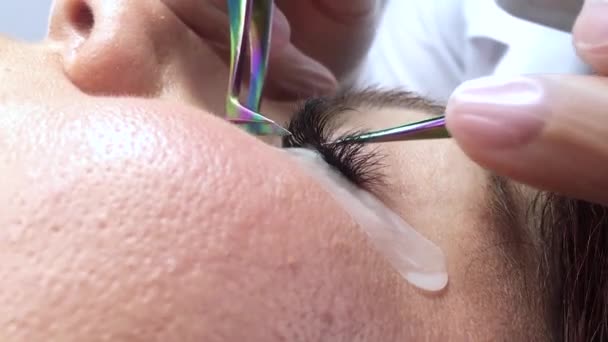 Unrecognizable woman eye close-up on eyelash extension procedure. Cropped video. The master checks his work for gluing. — Stock Video