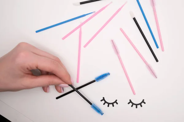 Vista superior de flatlay de las herramientas de extensión de pestañas. La mano femenina sostiene cepillos de colores para peinar cilios . — Foto de Stock