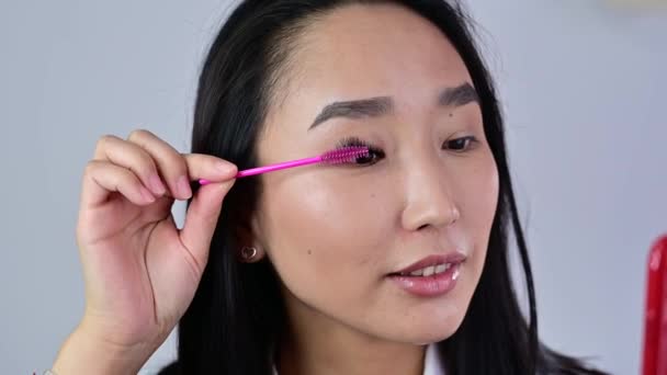 Asia menyikat bulu mata ekstensinya dengan kuas. Wanita dengan penutup mata yang akan datang make-up maskara. Industri kecantikan . — Stok Video