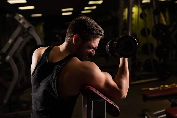 Un hombre guapo con gafas haciendo un ejercicio para bíceps con una barra. El tipo está involucrado en el culturismo. Entrenador en el gimnasio con brazos musculares . —  Fotos de Stock