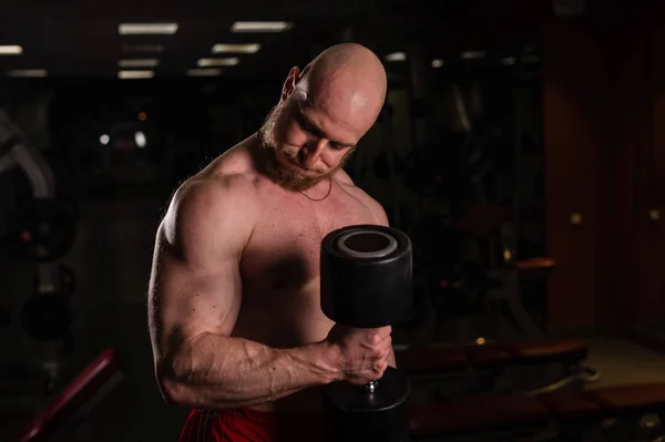 Póló nélküli jóképű férfi bicepsszel és tricepsszel tornázik súlyzóval. Dombornyomású testépítő, gyönyörű testtel. Izomtréner az edzőteremben. — Stock Fotó