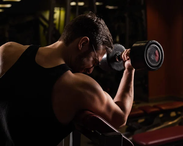 Gözlüklü yakışıklı bir adam halterle pazılar için egzersiz yapıyor. Adam vücut geliştirmekle meşgul. Spor salonunda kaslı kollarıyla antrenör.. — Stok fotoğraf