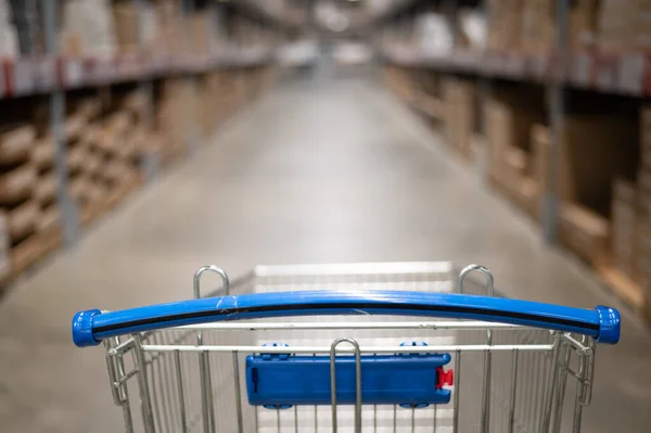 Carrinho de compras vazio em um armazém de loja de móveis. Supermercado shopping cesta corredor com caixa prateleira abstrato borrão desfocado fundo — Fotografia de Stock