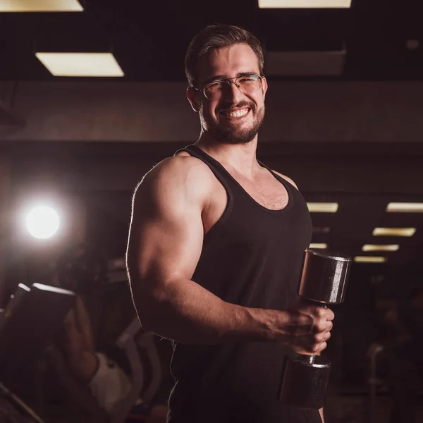 Een man met een inspanning doet een oefening voor biceps en triceps met een halter. Glimlachende bodybuilder met reliëf. Gespierde man met bril in de sportschool. — Stockfoto