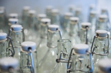 Bir şişenin boynuna yakın çekim. Tezgahtaki plastik kapaklı boş şişe grupları..