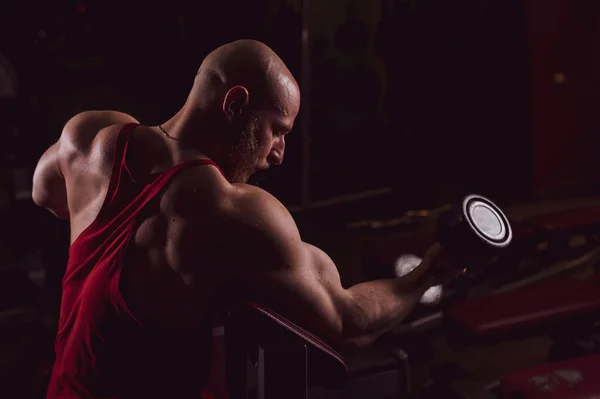 Glatzköpfiger Mann mit Bart macht Bizepsübungen. Der junge Mann betreibt Bodybuilding. Trainer im Fitnessstudio mit muskulösen Armen. — Stockfoto