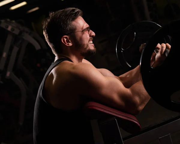 Hombre guapo con gafas haciendo ejercicio bíceps con mancuerna. El tipo inteligente está involucrado en el culturismo. Entrenador muscular en el gimnasio . —  Fotos de Stock