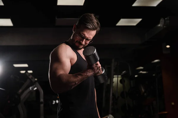 Egy férfi, akinek van erőfeszítése, bicepszeket és tricepszeket csinál súlyzóval. Dombornyomású testépítő. Izmos fickó szemüveggel az edzőteremben. — Stock Fotó