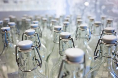 Bir şişenin boynuna yakın çekim. Tezgahtaki plastik kapaklı boş şişe grupları..