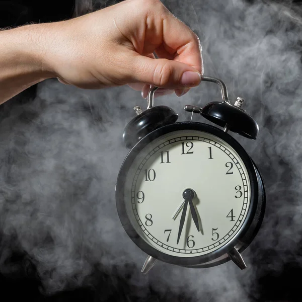 Una mujer sostiene un despertador en un estudio lleno de humo. Niebla blanca envolvió un reloj mecánico retro redondo . —  Fotos de Stock