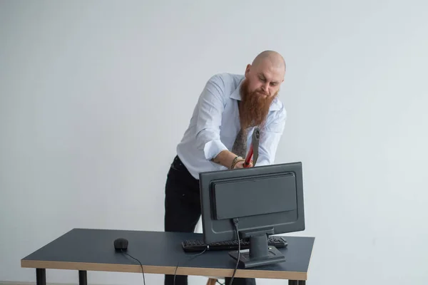 Arg skallig man med rött skägg på kontoret i kostym krossar en yxa med en dator. Chefen med ett nervöst sammanbrott, bryter bildskärmen. — Stockfoto