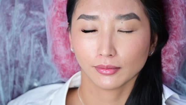 Retrato de uma bela mulher asiática abre os olhos durante o procedimento de extensão da pestana. Volume de pestanas duplas antes e depois . — Vídeo de Stock